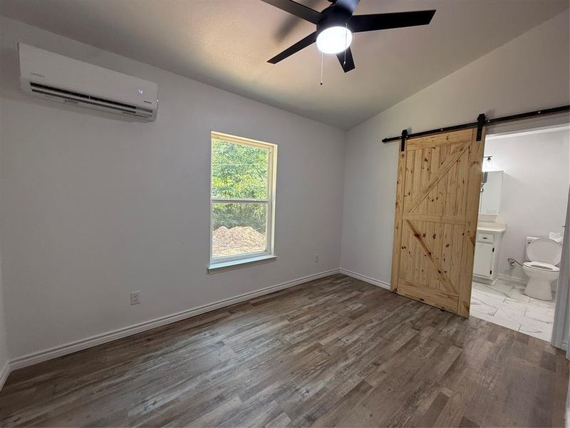 Unfurnished bedroom featuring a barn door, lofted ceiling, wood finished floors, an AC wall unit, and a ceiling fan