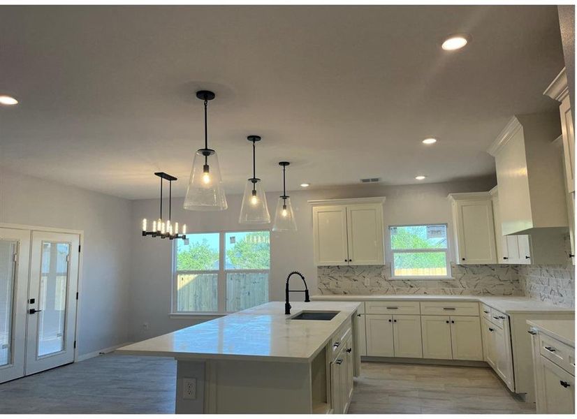 Kitchen featuring a center island with sink, backsplash, light hardwood / wood-style flooring, sink, and decorative light fixtures