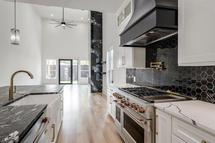 Kitchen with dark stone countertops, stainless steel appliances, white cabinetry, custom range hood, and backsplash Kitchen with dark stone countertops, stainless steel appliances, white cabinetry, custom range hood, and backsplash