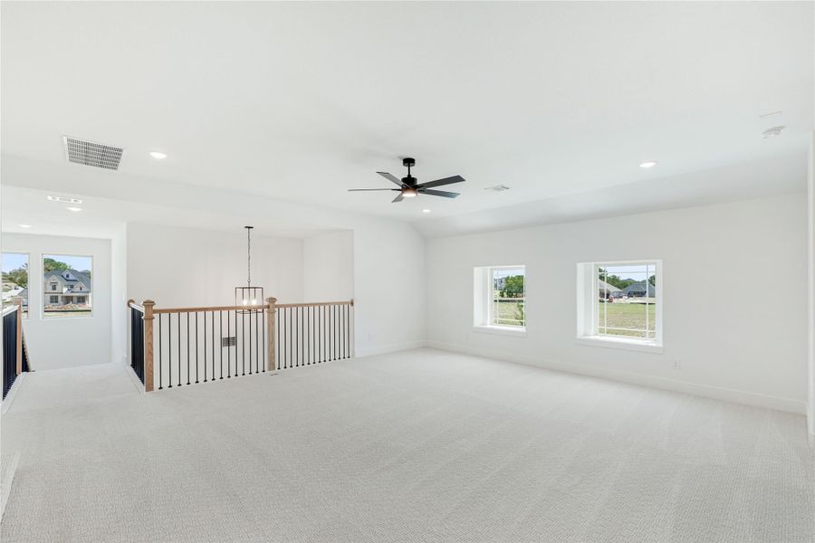 Open upstairs loft with carpet flooring, ceiling fan, and metal stair railing overlooking lower level