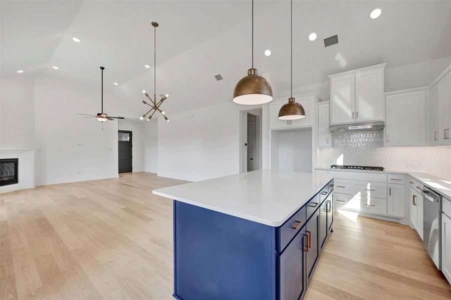 Two tone kitchen with two tone cabinetry, light wood-style flooring, a center island, a glass covered fireplace, and tasteful backsplash Two tone kitchen with two tone cabinetry, light wood-style flooring, a center island, a glass covered fireplace, and tasteful backsplash