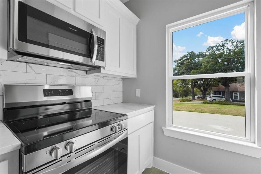 Kitchen featuring light stone countertops, appliances with stainless steel finishes, tasteful backsplash, and white cabinetry