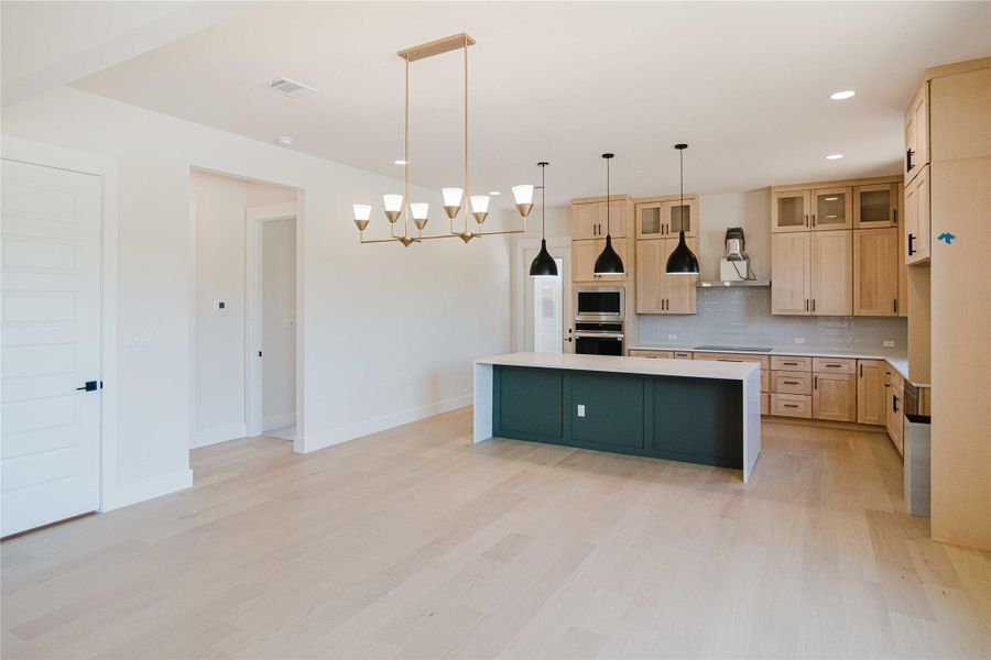 Kitchen with a kitchen island, a chandelier, glass insert cabinets, light brown cabinets, and decorative light fixtures