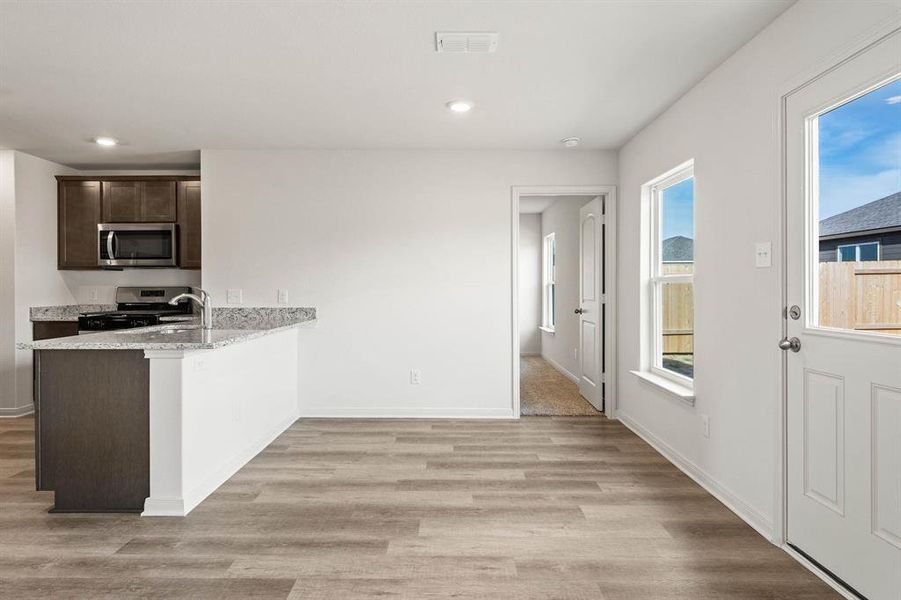 Kitchen featuring light wood-type flooring, stainless steel appliances, kitchen peninsula, light stone counters, and dark brown cabinetry