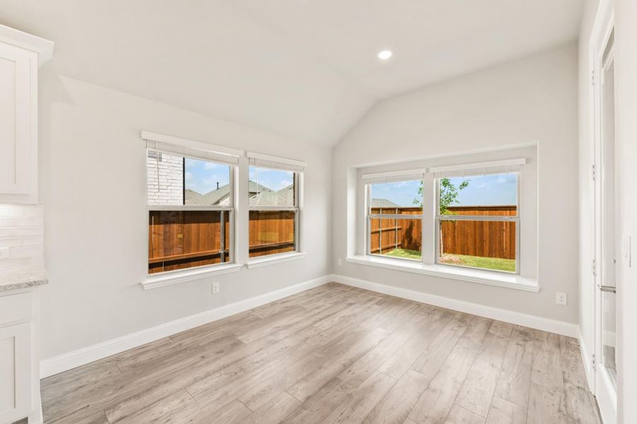 Empty room with vaulted ceiling, light wood floors, and large windows overlooking a fenced backyard Empty room with vaulted ceiling, light wood floors, and large windows overlooking a fenced backyard