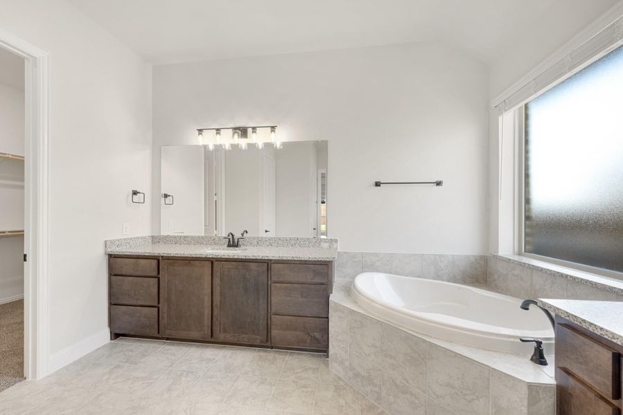 Master bathroom with dark wood vanity, granite countertop, soaking tub, and tile surround next to a frosted window Master bathroom with dark wood vanity, granite countertop, soaking tub, and tile surround next to a frosted window