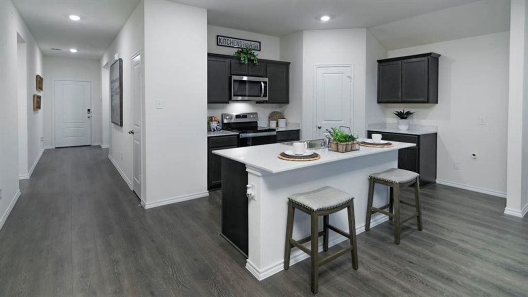 Kitchen featuring stainless steel appliances, a kitchen island with sink, a breakfast bar, dark wood-type flooring, and recessed lighting