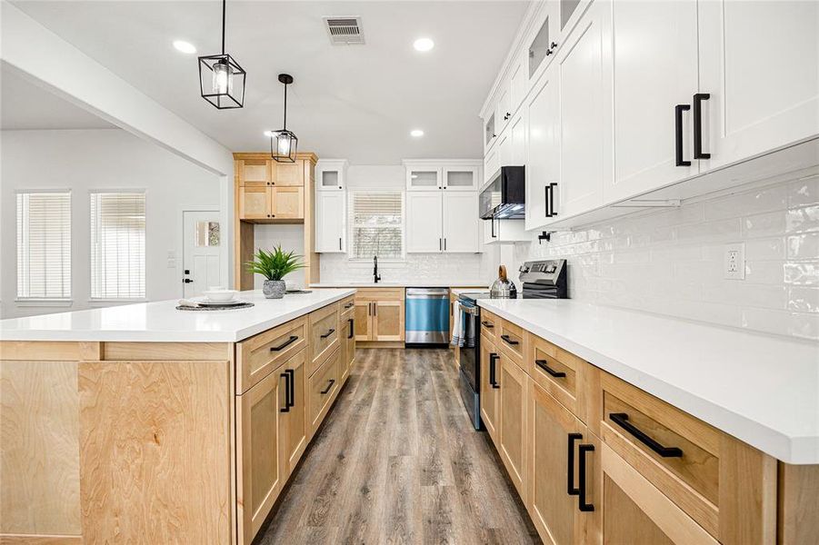 This kitchen features a modern design with white and natural wood cabinetry, sleek black hardware, and stainless steel appliances. The space is bright and open, with pendant lighting, a large island, and a stylish subway tile backsplash.