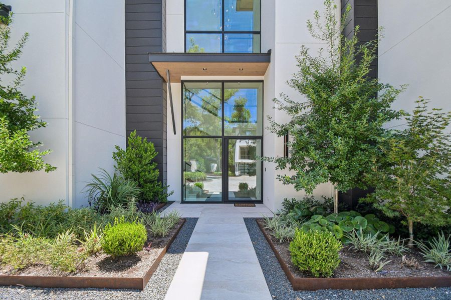 Symmetrical pathways and manicured garden beds frame this modern multi-story glass entryway. Symmetrical pathways and manicured garden beds frame this modern multi-story glass entryway.