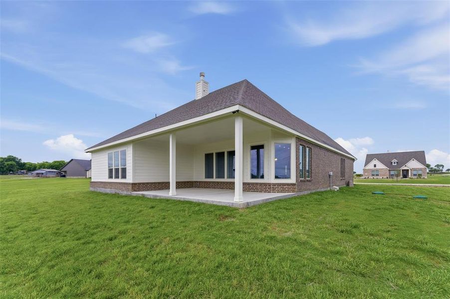 The property features a spacious covered patio, a well-maintained lawn, and a facade with brick and siding