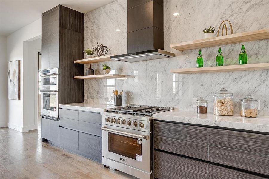 Kitchen featuring open shelves, stainless steel appliances, decorative backsplash, wall chimney range hood, and modern cabinets