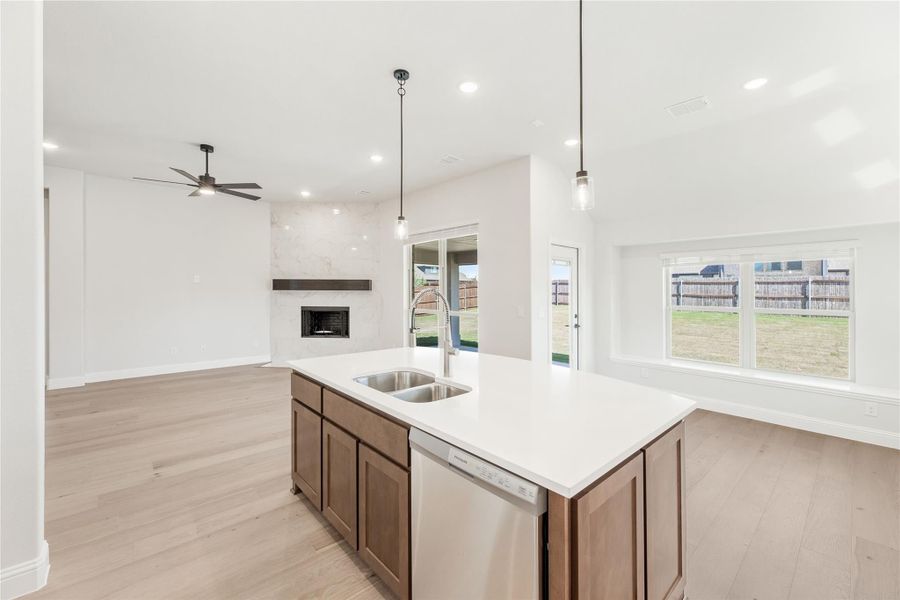 Kitchen island with double sink and dishwasher, open to living room with fireplace and hardwood floors