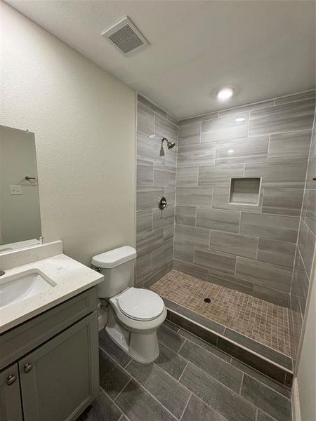 Bathroom featuring a tile shower, vanity, and toilet