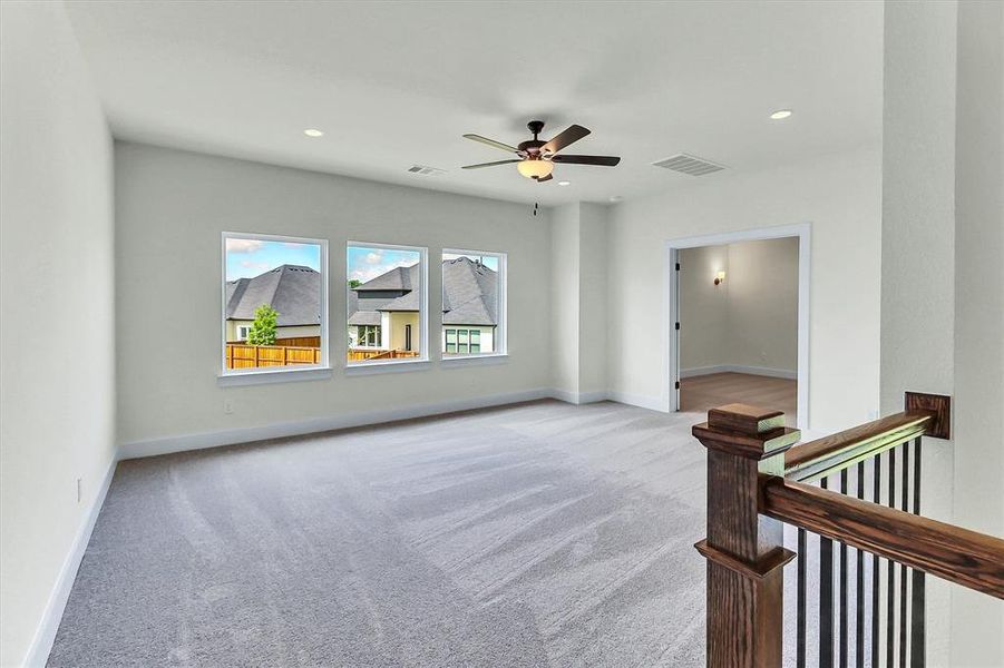 Spacious carpeted room featuring three large windows, a ceiling fan with integrated lighting, and recessed lighting Spacious carpeted room featuring three large windows, a ceiling fan with integrated lighting, and recessed lighting