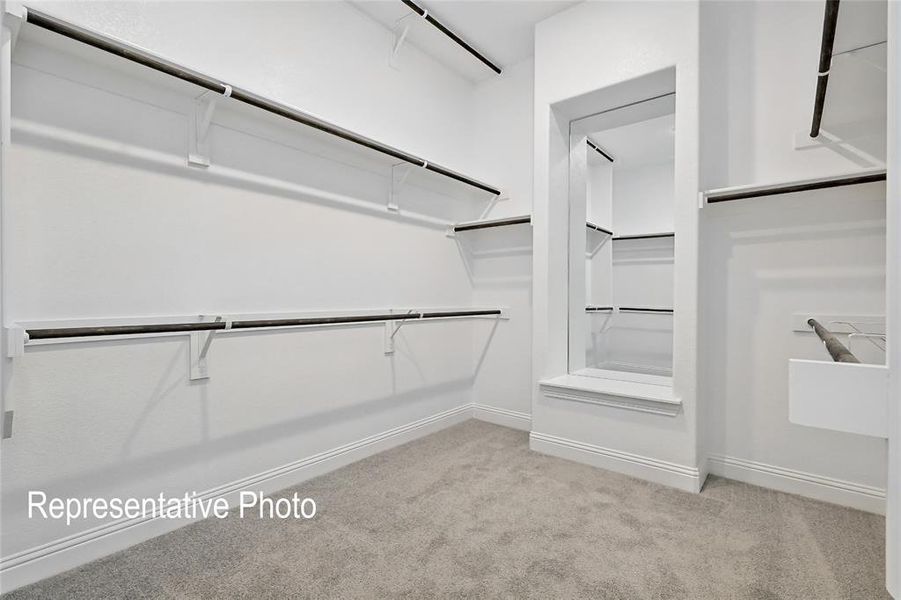 Spacious walk-in closet featuring extensive shelving, multiple hanging rods, a built-in mirror, and light gray carpet flooring