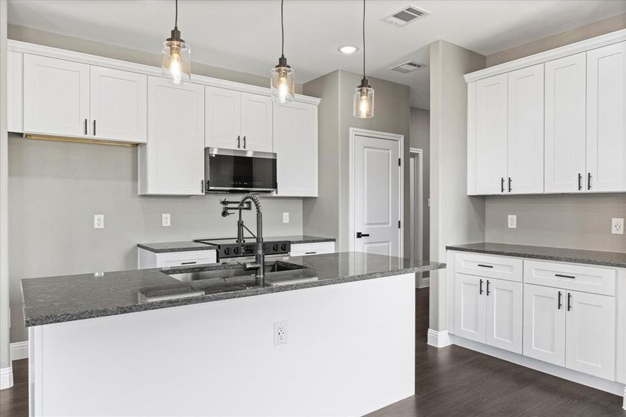 Kitchen featuring white cabinetry, dark stone counters, decorative light fixtures, and a center island with sink