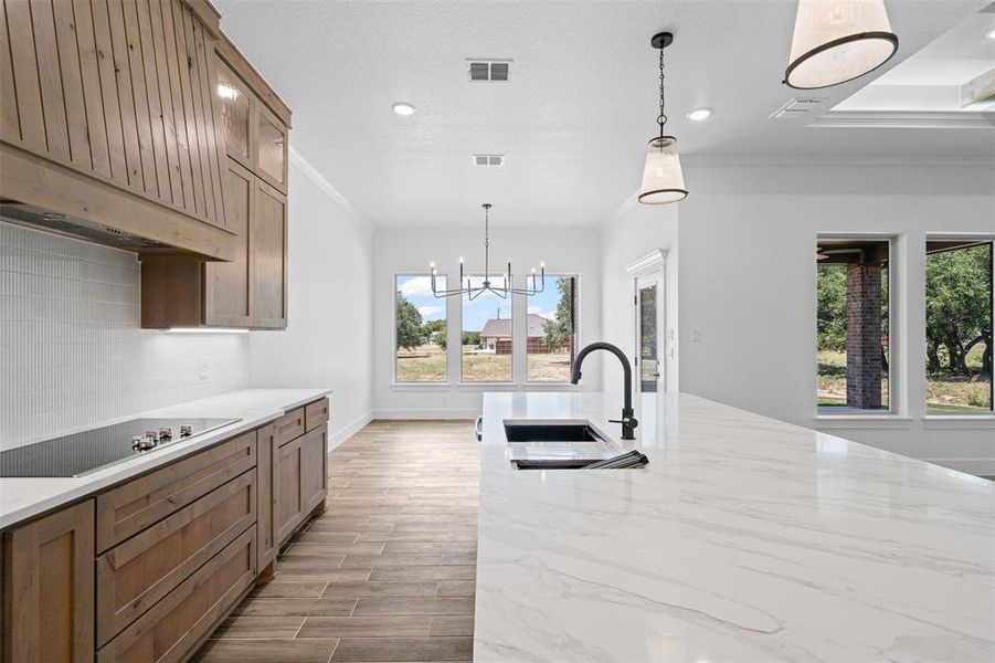 Kitchen featuring crown molding, range hood, light wood finished floors, black electric cooktop, and a chandelier Kitchen featuring crown molding, range hood, light wood finished floors, black electric cooktop, and a chandelier