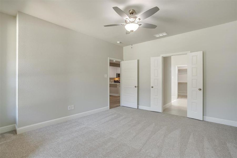 Unfurnished bedroom with light colored carpet, a walk in closet, and ceiling fan Unfurnished bedroom with light colored carpet, a walk in closet, and ceiling fan