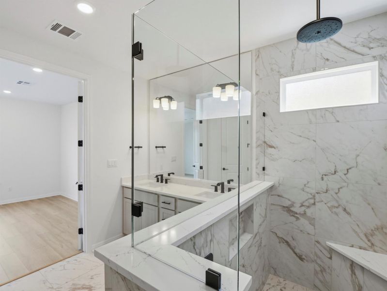 A well-appointed primary bathroom showcases dual vanities and a spacious walk-in shower with marble-look tile. A well-appointed primary bathroom showcases dual vanities and a spacious walk-in shower with marble-look tile.