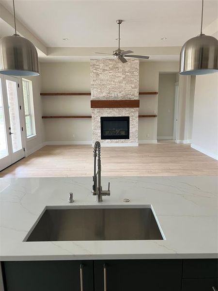 Kitchen with a stone fireplace, sink, hanging light fixtures, built in shelves, and light stone counters