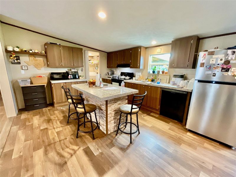 Kitchen featuring a central island with stone-look facade, wood-finish flooring, wood cabinetry, light-toned countertops, and recessed lighting