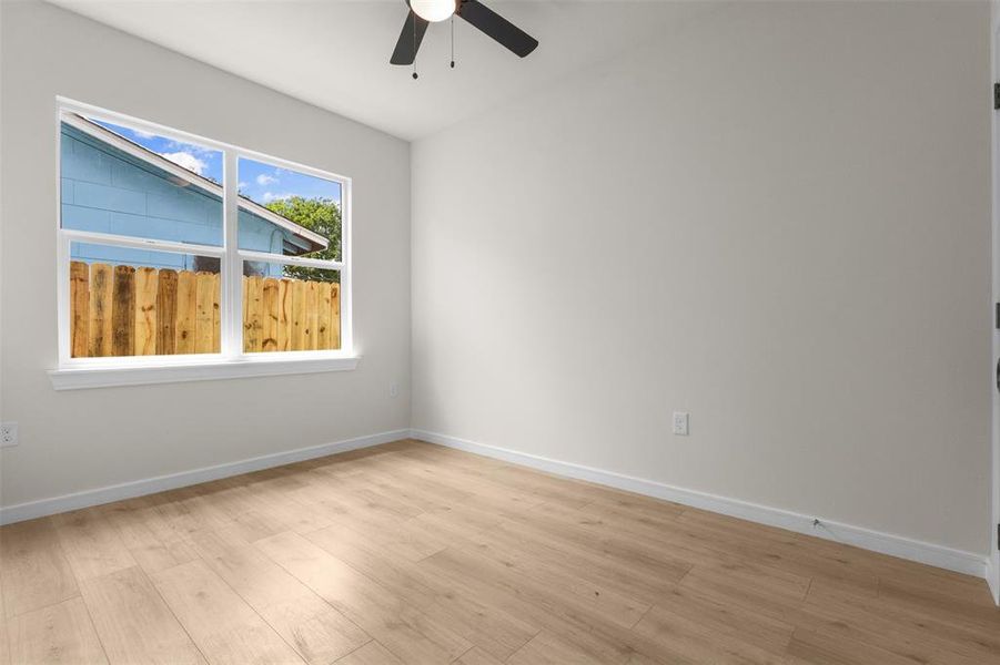 Room featuring wood-finish flooring, a ceiling fan, a large window with white trim, white baseboards, and light-colored walls