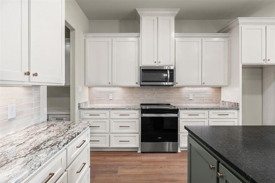 Kitchen featuring stainless steel appliances, white cabinets, dark stone counters, and tasteful backsplash