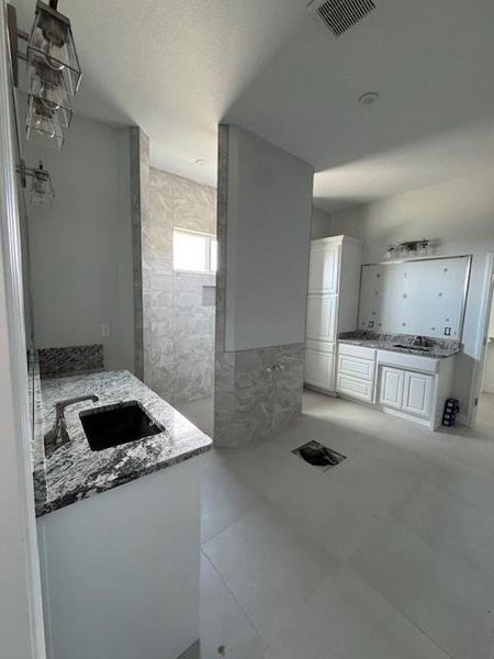 Bathroom featuring two vanities, a textured ceiling, walk in shower, and tile walls