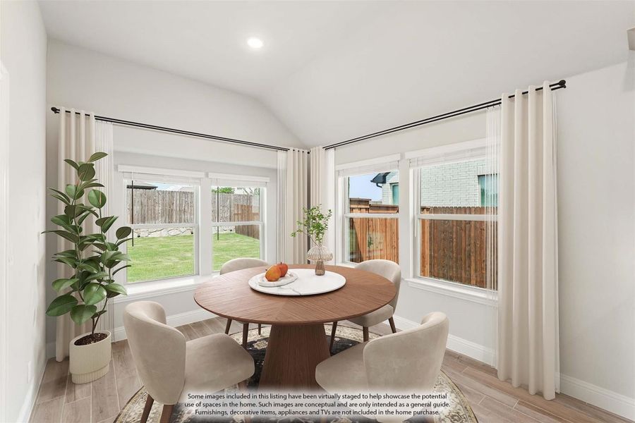 Bright dining nook with round wood table, four chairs, vaulted ceiling, and large windows overlooking backyard.
