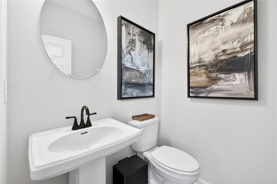 Pedestal sink with black faucet, round wall mirror, and white toilet