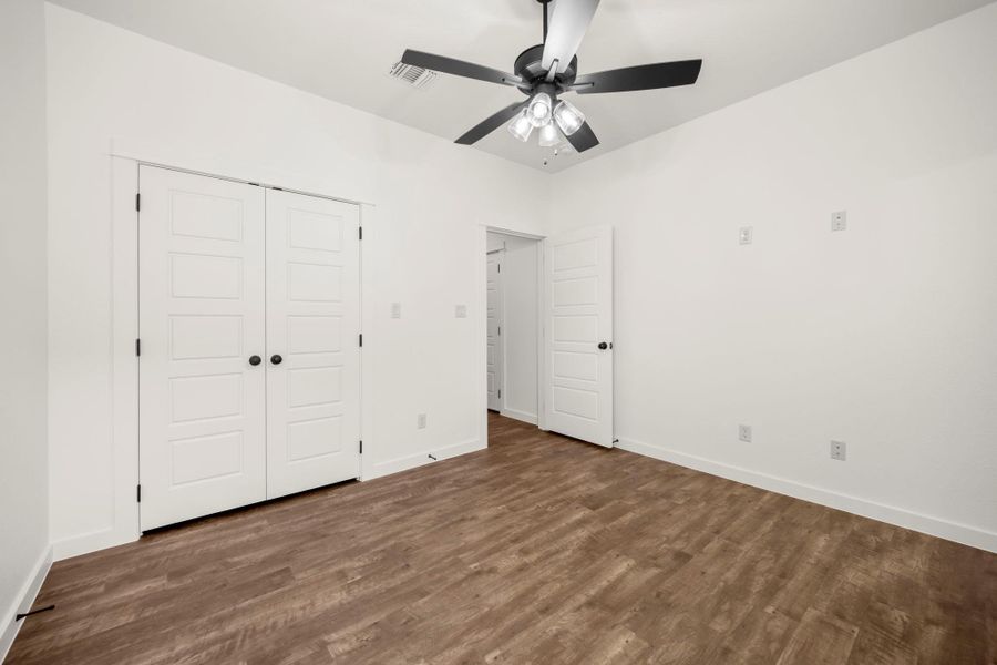 A well-lit bedroom with modern vinyl flooring, double closet doors, and a functional ceiling fan.