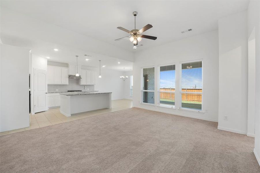 Unfurnished living room featuring ceiling fan with notable chandelier, sink, and light colored carpet