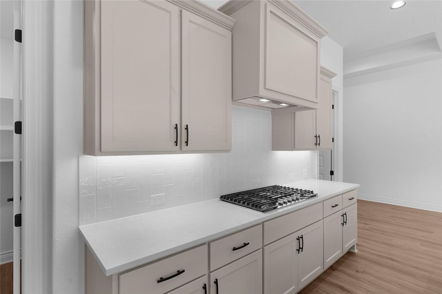 Kitchen with light wood-type flooring, stainless steel gas cooktop, white cabinetry, backsplash, and recessed lighting