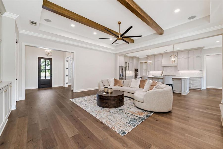 Living area featuring dark wood finished floors, ornamental molding, a ceiling fan, beamed ceiling, and a raised ceiling Living area featuring dark wood finished floors, ornamental molding, a ceiling fan, beamed ceiling, and a raised ceiling