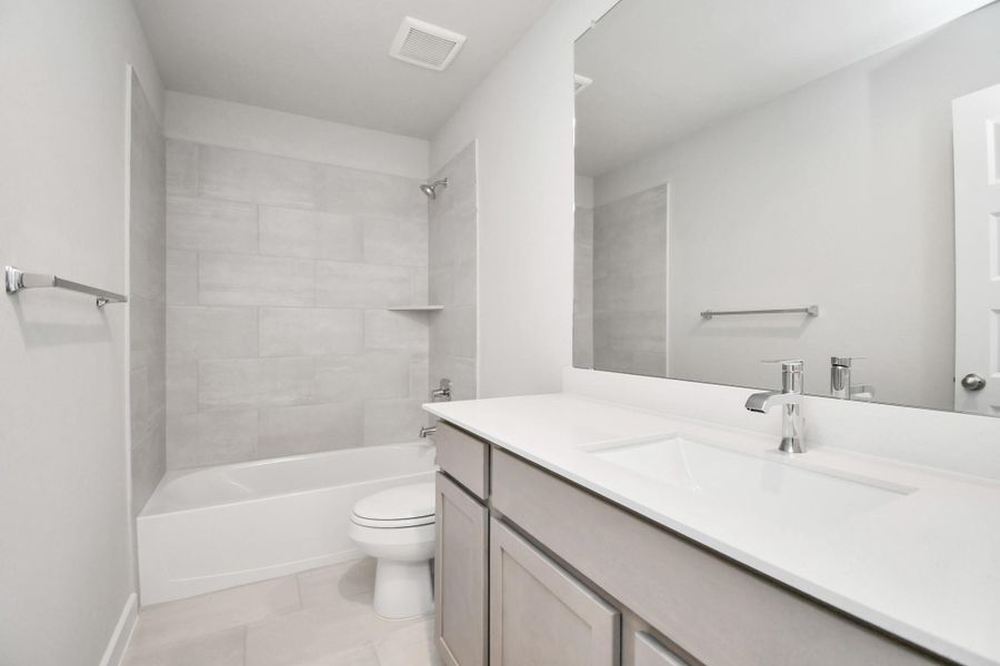 Secondary bath features tile flooring, bath/shower combo with tile surround, light stained wood cabinets, beautiful light countertop. Sample photo of completed home with similar floor plan. Actual colors and selections may vary.