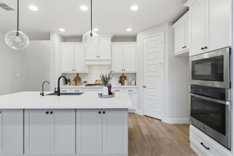 A large center island anchors the kitchen, providing ample workspace, additional storage, and casual seating. Built-in stainless steel wall ovens, expansive cabinetry, and clean architectural lines deliver both elegance and exceptional functionality.