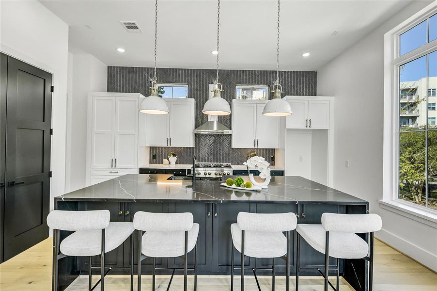 This chef-inspired kitchen features a harmonious mix of black and white custom cabinetry, polished hardware, and a statement full-wall backsplash. The expansive island with bar seating offers the perfect gathering spot, illuminated by designer pendant lights and surrounded by picture windows framing lush outdoor views. This chef-inspired kitchen features a harmonious mix of black and white custom cabinetry, polished hardware, and a statement full-wall backsplash. The expansive island with bar seating offers the perfect gathering spot, illuminated by designer pendant lights and surrounded by picture windows framing lush outdoor views.