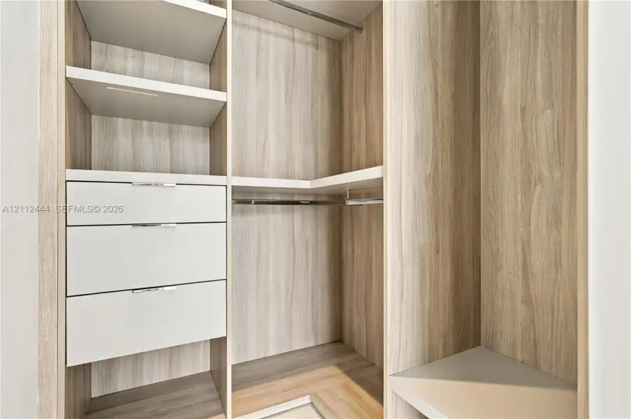 Custom walk-in closet featuring wood-finish cabinetry, open shelving, integrated drawers with metal pulls, and built-in hanging rods