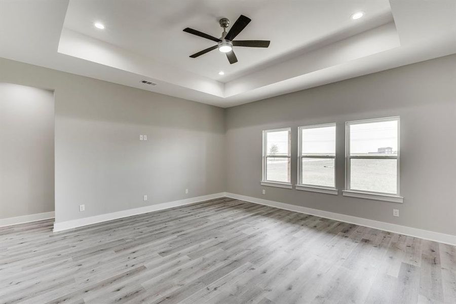 Spare room featuring ceiling fan, light hardwood / wood-style flooring, and a tray ceiling