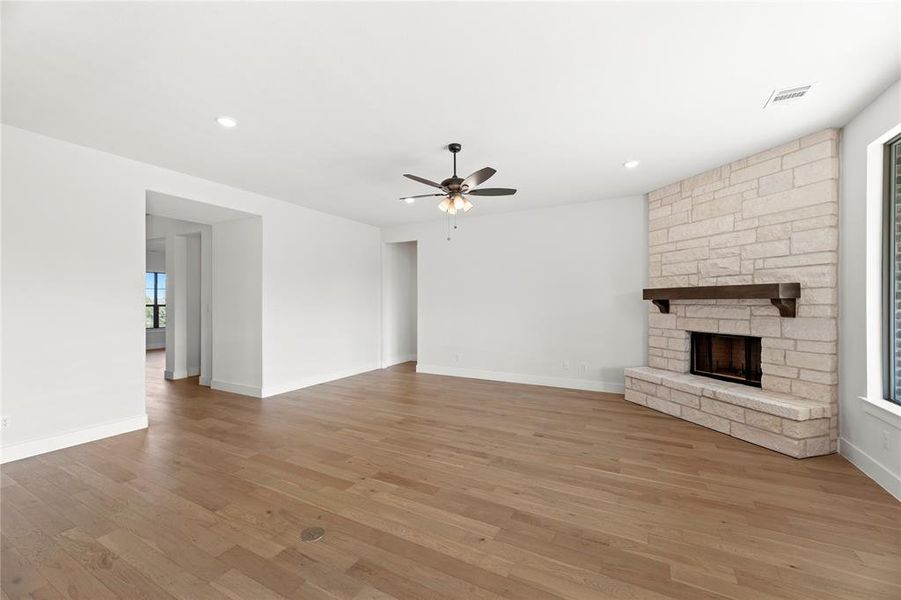 Unfurnished living room featuring a stone fireplace, light hardwood / wood-style floors, and ceiling fan