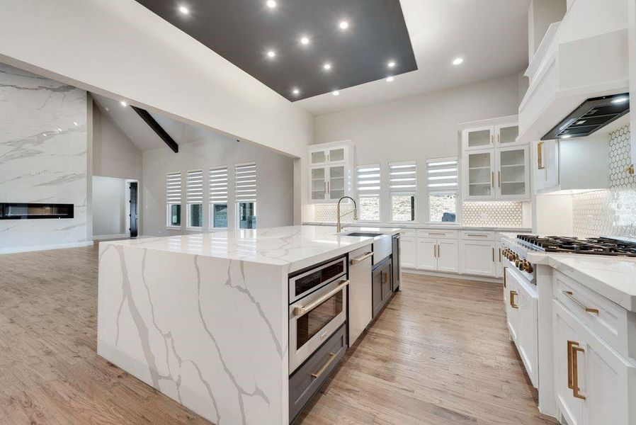 Kitchen featuring appliances with stainless steel finishes, light stone countertops, premium range hood, a spacious island, and white cabinetry