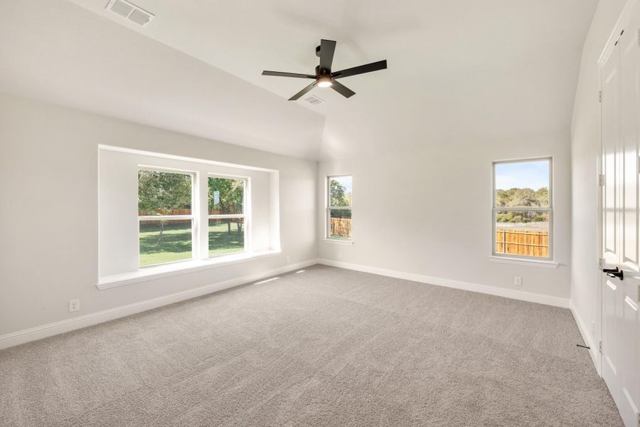 Empty bedroom with gray carpet, ceiling fan, and multiple windows overlooking a backyard