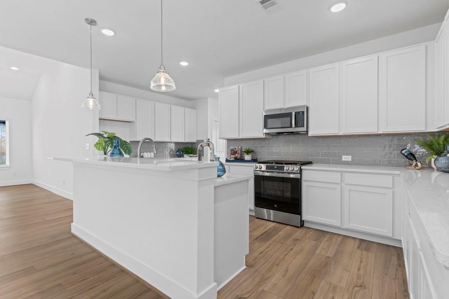 Another view of the kitchen highlights its seamless connection to the living areas, abundance of cabinet space, freestanding gas range, built-in microwave, and modern finishes—ideal for everyday living and entertaining. **Image Representative of Plan Only and May Vary as Built**.