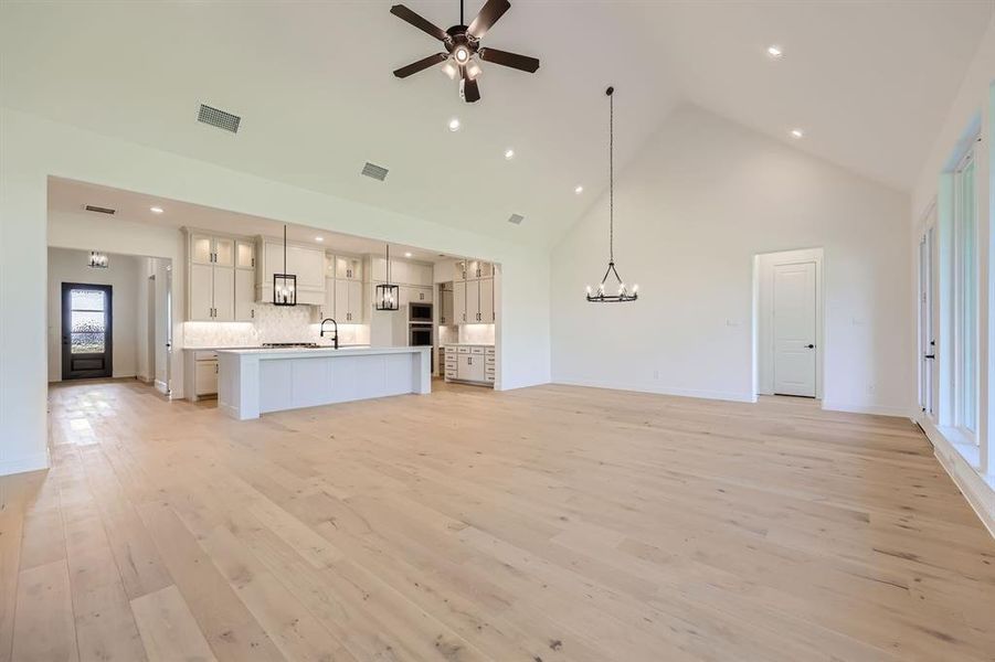 Unfurnished living room with high vaulted ceiling, ceiling fan with notable chandelier, sink, and light hardwood / wood-style flooring