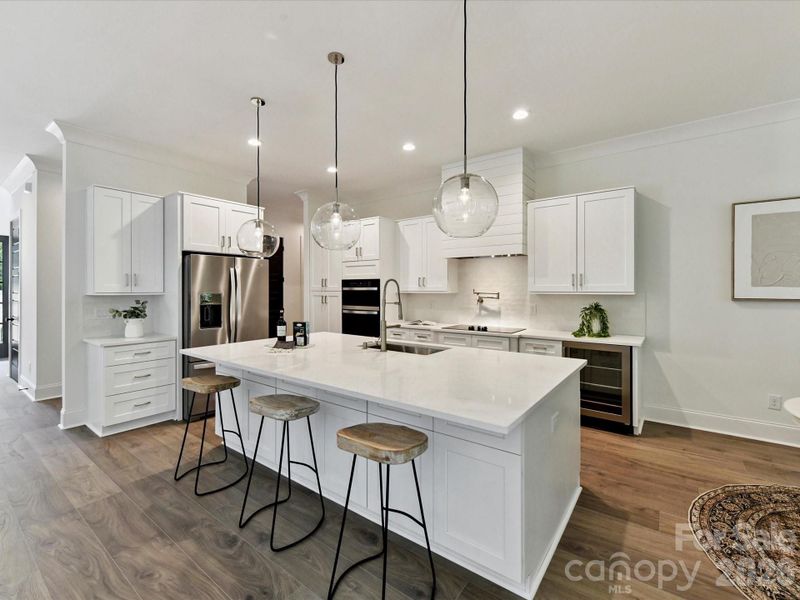 Designer kitchen featuring a large quartz island with seating, custom cabinetry, stainless steel appliances, and stylish pendant lighting.