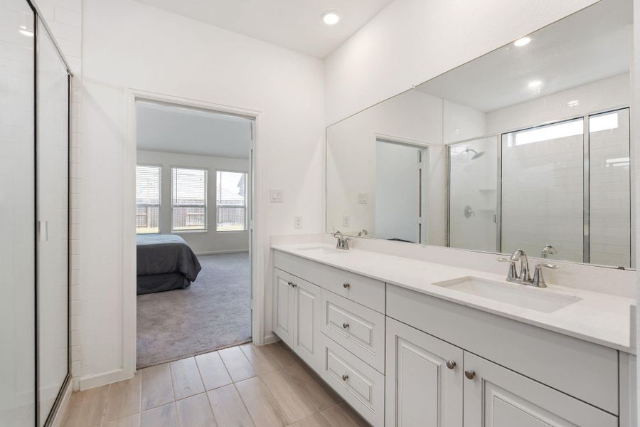 Luxury primary ensuite in white, with upgraded raised panel cabinetry, solid surface countertops, undermount double sinks, tile floors, large tile shower, linen closet, and a massive walk-in closet!
