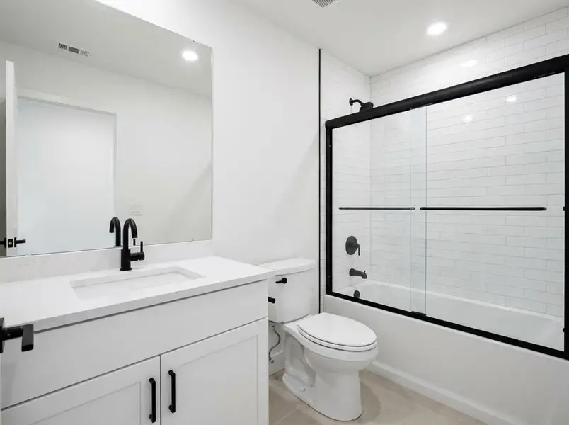 Bathroom featuring a white vanity with a light-toned countertop, black fixtures, and a white subway tile tub surround with a black-framed glass shower door