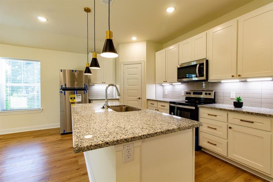 Kitchen featuring stainless steel appliances, light wood-style flooring, an island with sink, decorative backsplash, and white cabinets Kitchen featuring stainless steel appliances, light wood-style flooring, an island with sink, decorative backsplash, and white cabinets