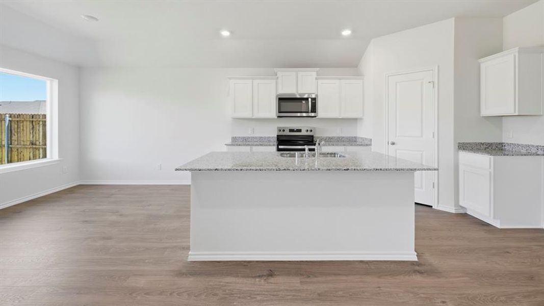 Kitchen with light stone counters, white cabinetry, stainless steel appliances, a kitchen island with sink, and dark wood finished floors