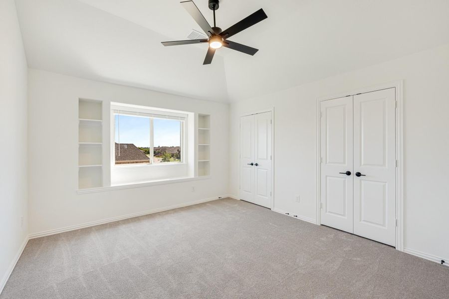 Empty bedroom with vaulted ceiling, ceiling fan, built-in shelves, and two white double doors Empty bedroom with vaulted ceiling, ceiling fan, built-in shelves, and two white double doors